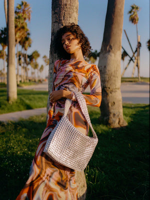 alt=woman at venice beach leaning against palm tree with a silver pop tab purse by escama studio