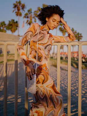 alt="silver crossbody cell phone bag made from pop tabs worn by woman on balcony over looking beach  wearing orange psychedlic maxi dress"