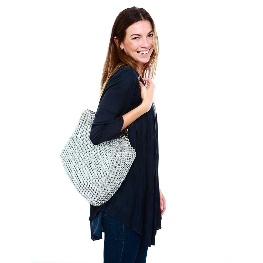 alt="silver woven tote made of recycled pop tabs worn by smiling woman, Kate tote by Escama Studio"